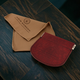 A dark red leather card holder wallet and a tan microfiber cleaning cloth from Noir Garcon, displayed on a dark wood tabletop.