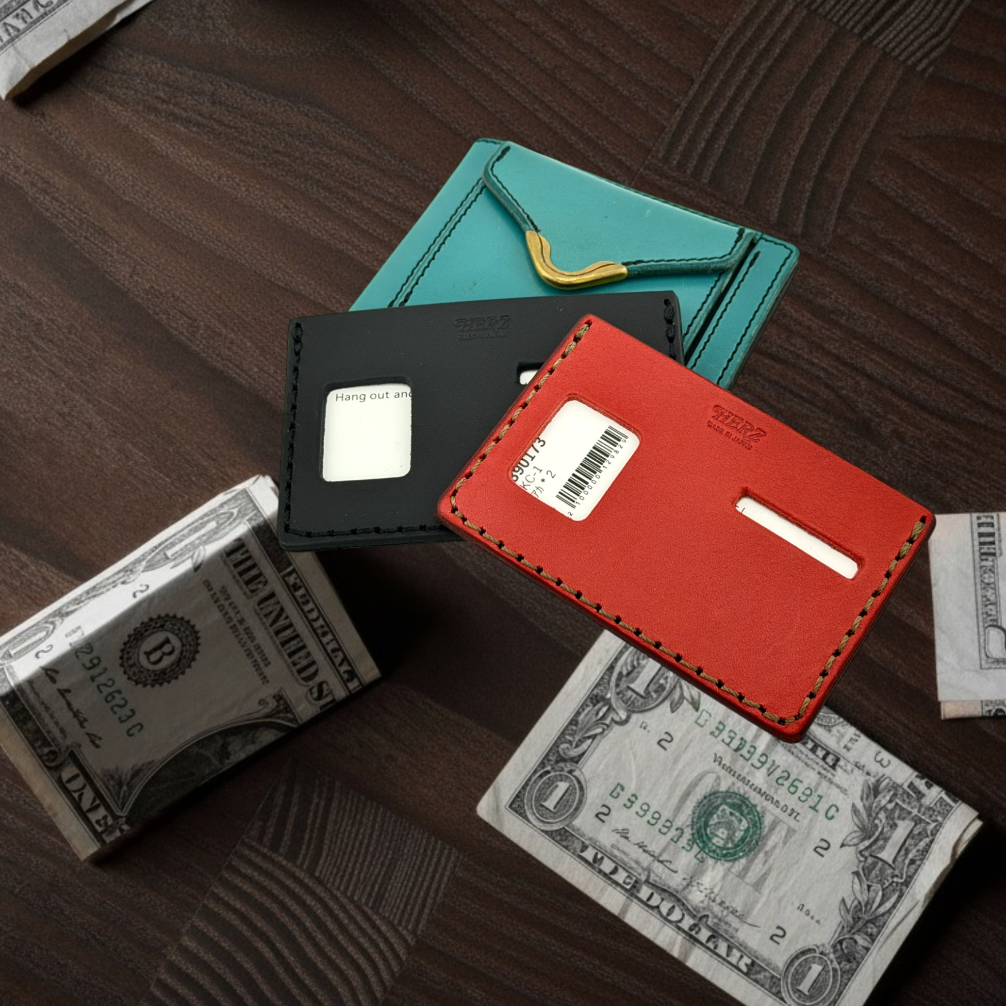 Three cardholders in black, red, and teal on a wooden surface with dollar bills.
