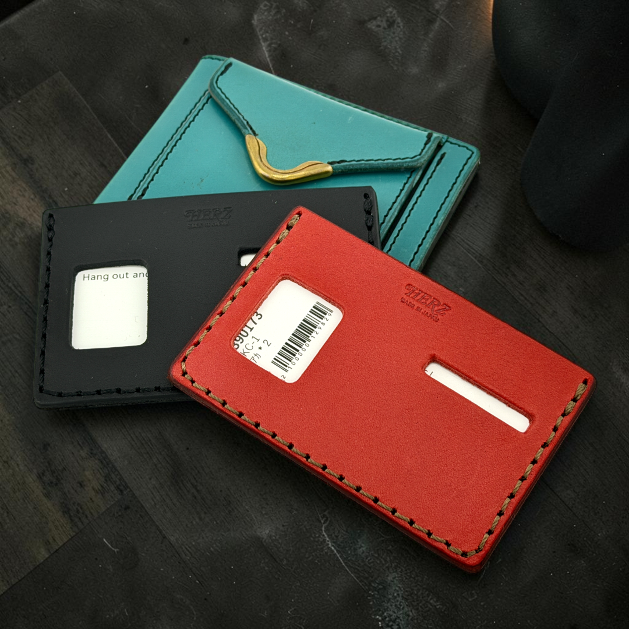Three leather card holders in black, red, and teal on a dark surface.