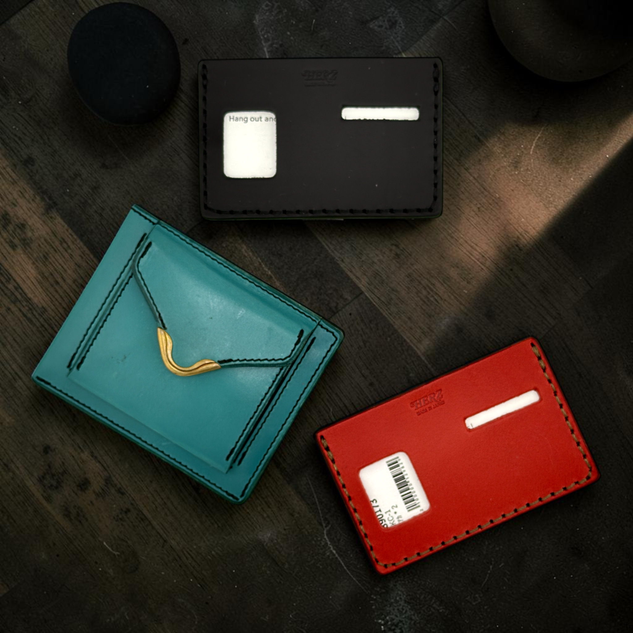 Three cardholders in black, teal, and red on a dark wooden surface.