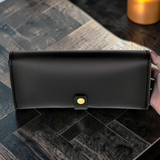 Black leather bag with a yellow button held on a wooden surface