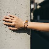 TagSthx coral leather watch strap with V-stitch detail worn on a wrist against a concrete wall