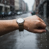 Hand wearing a watch with raindrops on a blurred background