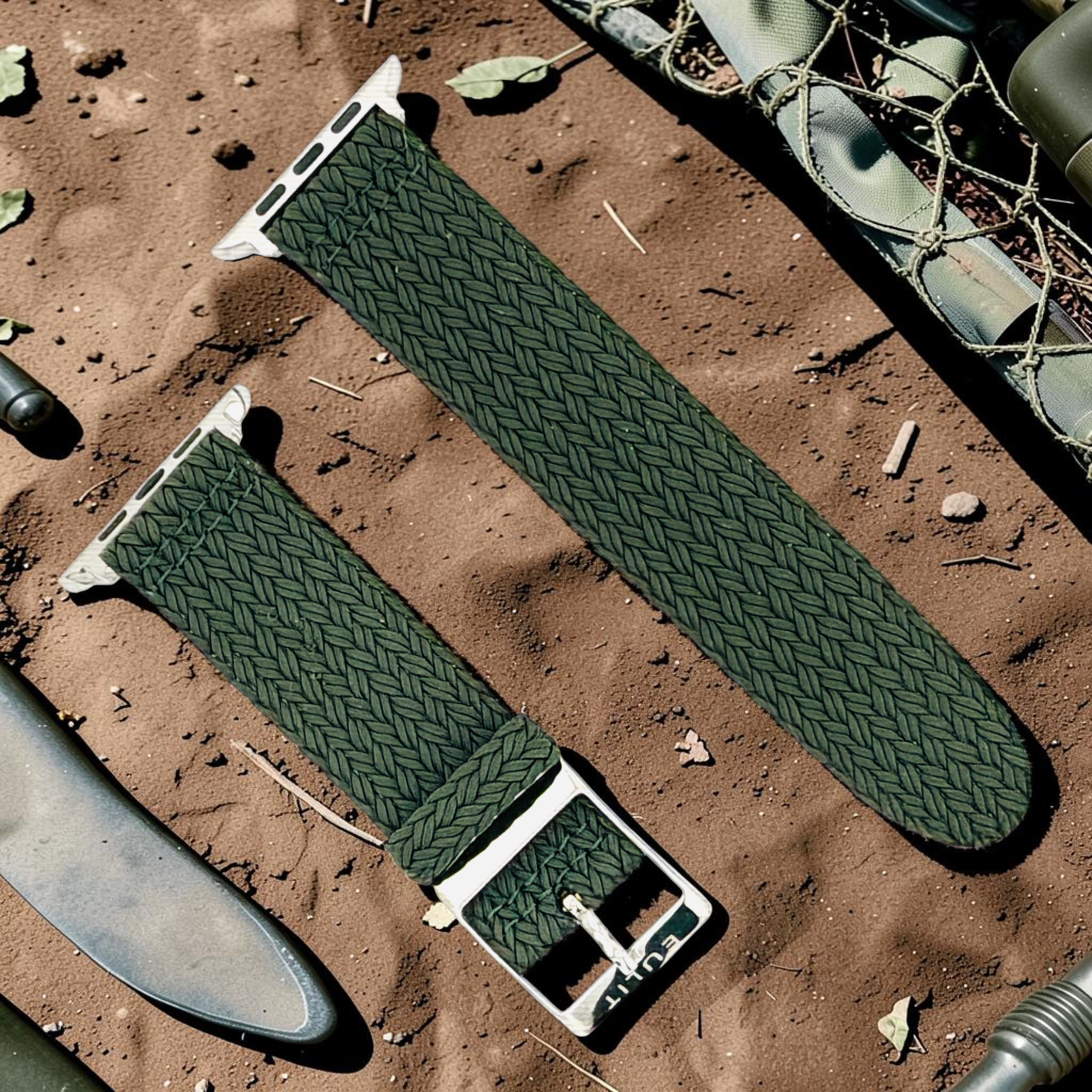 Green woven watch strap on a sandy surface with military equipment in the background