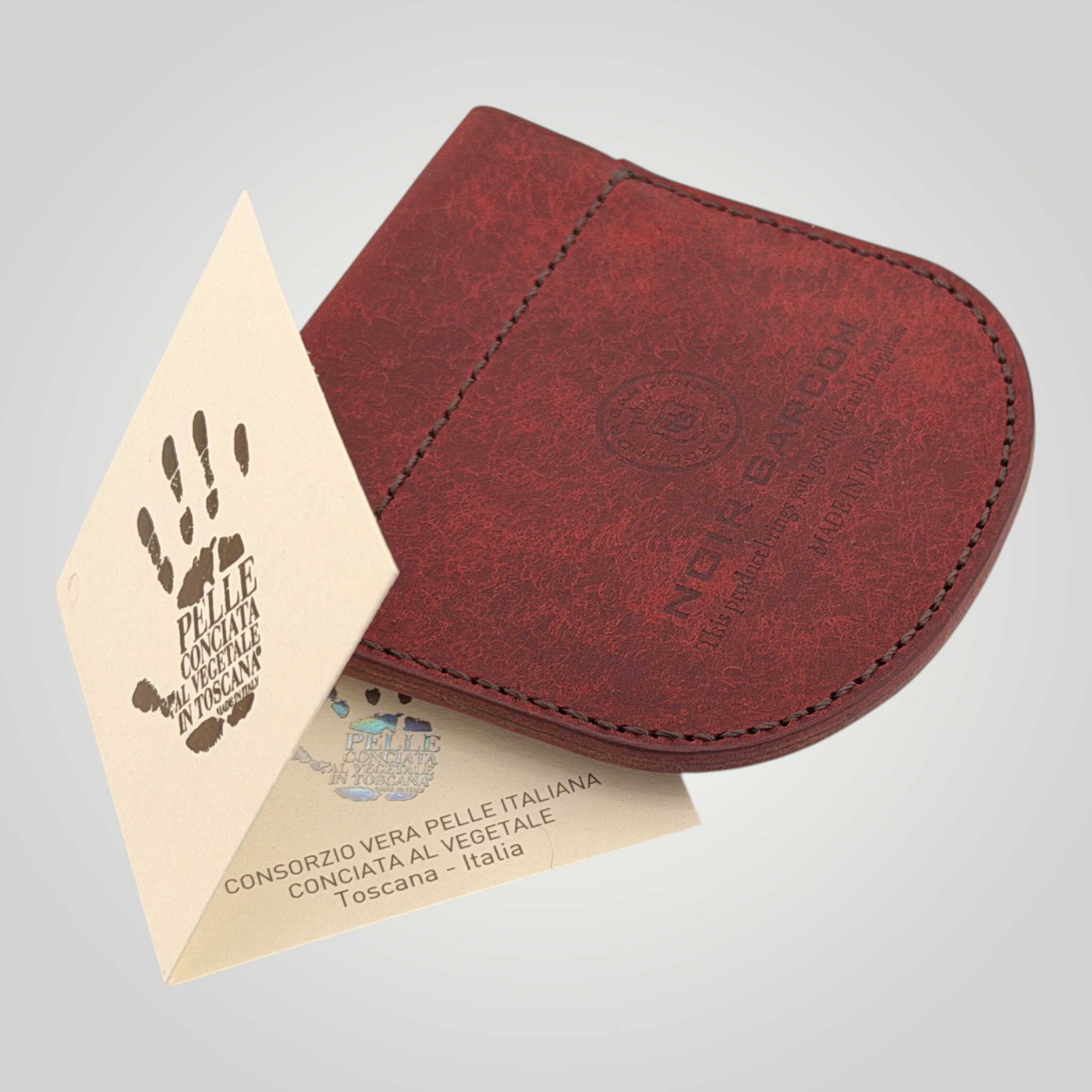 A dark red leather card holder or wallet with a rounded bottom and visible stitching, shown on a light gray background with branded paper inserts.