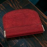 A red leather card holder wallet with silver metal clasps, resting on a dark wood surface.