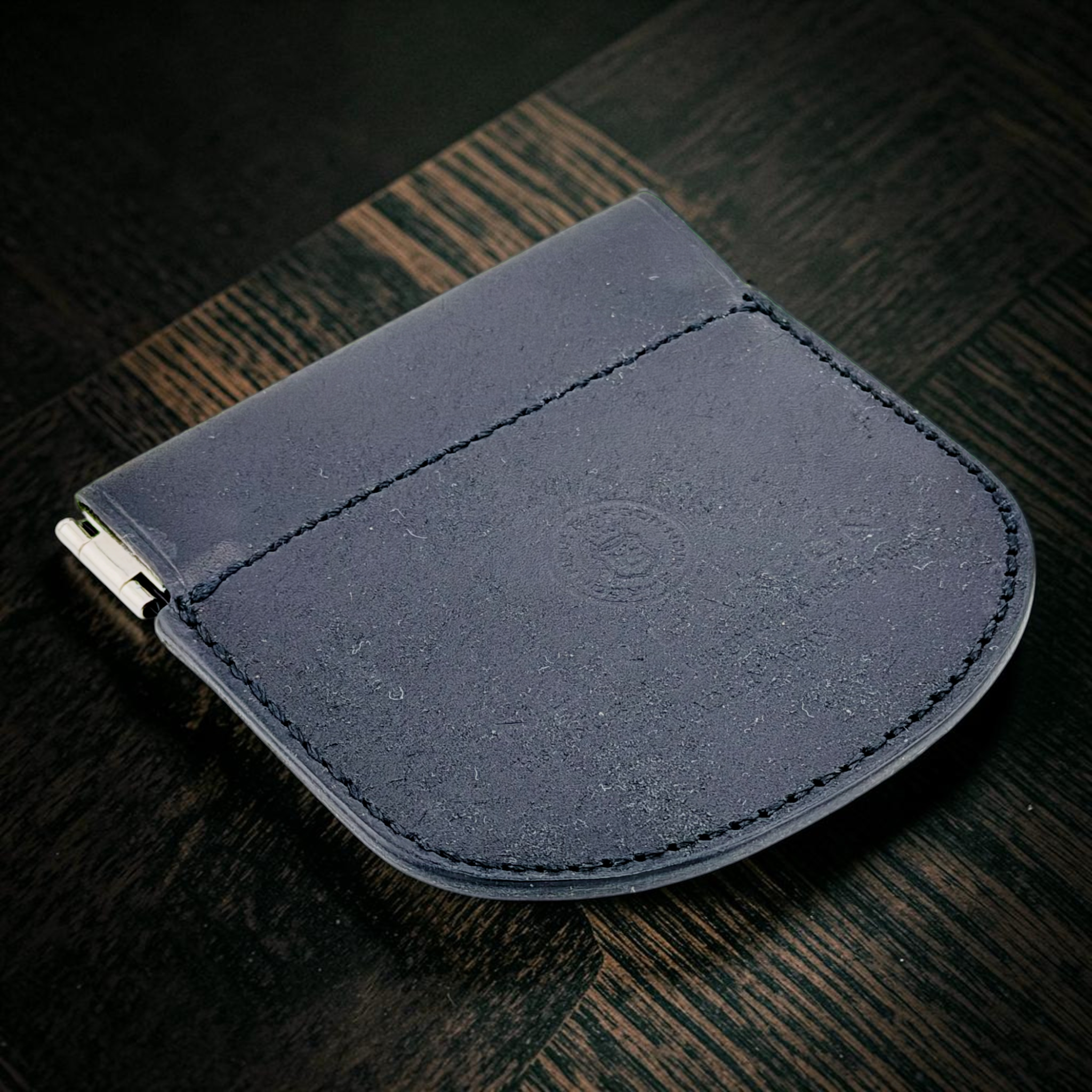 A dark navy blue leather card holder or wallet with a metal clip on the side, resting on a dark wood surface.