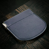 A dark navy blue leather card holder or wallet with a metal clip on the side, resting on a dark wood surface.